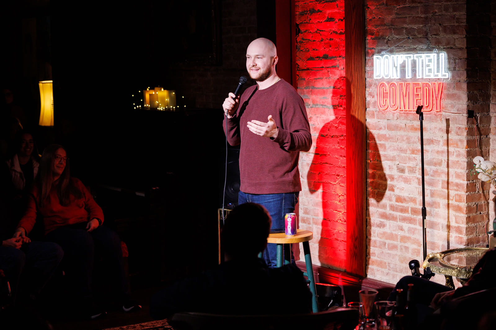 Gabe Gerry performing standup comedy on stage in front of a neon "Don't Tell Comedy" sign